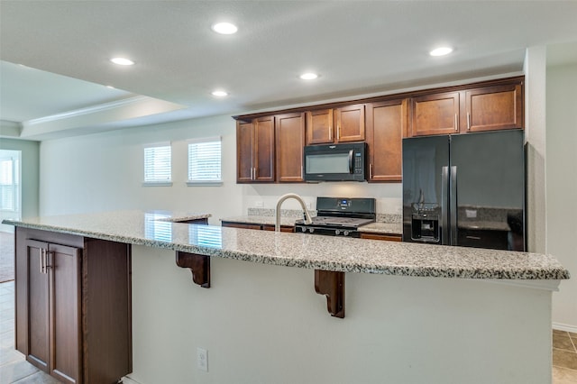 kitchen featuring a center island with sink, ornamental molding, black appliances, light stone countertops, and a kitchen bar