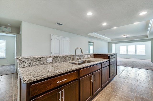 kitchen featuring sink, light colored carpet, a raised ceiling, and a center island with sink