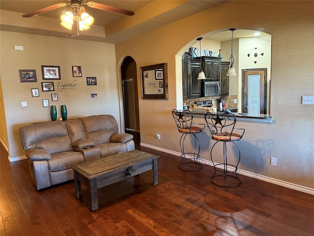 living room featuring ceiling fan, a tray ceiling, and dark hardwood / wood-style floors