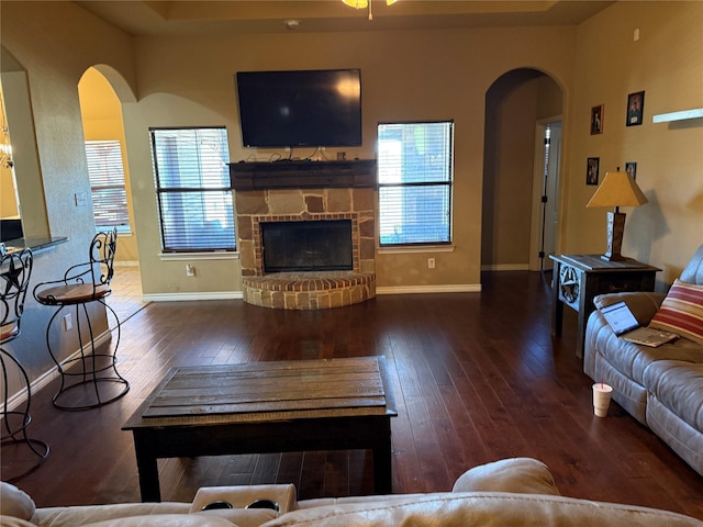 living room featuring a raised ceiling, dark wood-type flooring, a wealth of natural light, and a fireplace