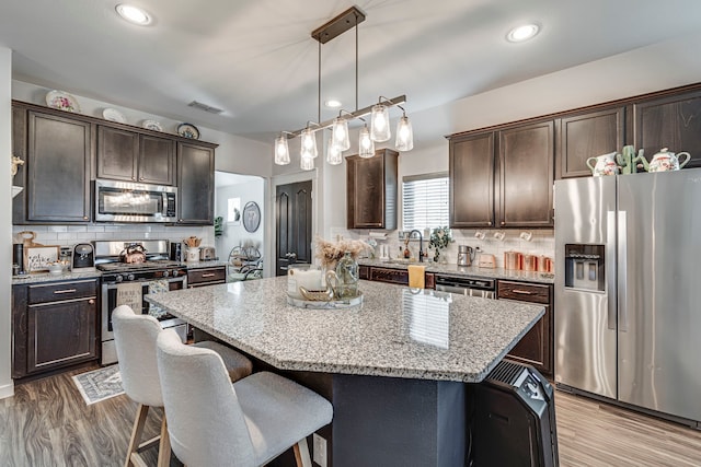 kitchen featuring dark brown cabinetry, appliances with stainless steel finishes, a breakfast bar, and visible vents