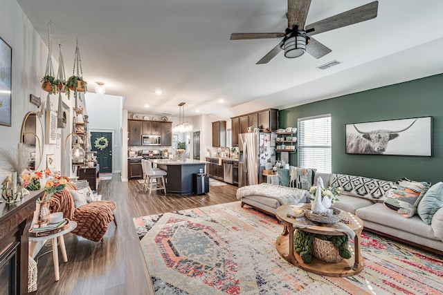 living area featuring visible vents, recessed lighting, dark wood-style flooring, and ceiling fan with notable chandelier