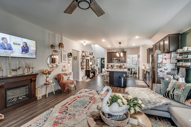 living area featuring ceiling fan, a glass covered fireplace, baseboards, and dark wood-type flooring