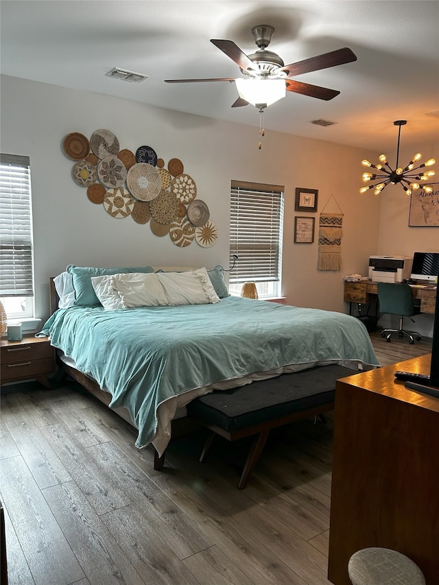 bedroom with visible vents, ceiling fan with notable chandelier, and hardwood / wood-style floors