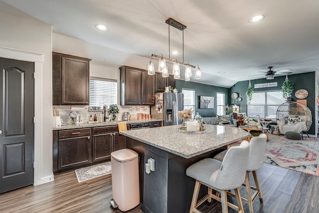 kitchen with a kitchen breakfast bar, dark brown cabinets, a sink, open floor plan, and stainless steel fridge