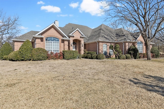 view of front of home with a front lawn, brick siding, a chimney, and a shingled roof