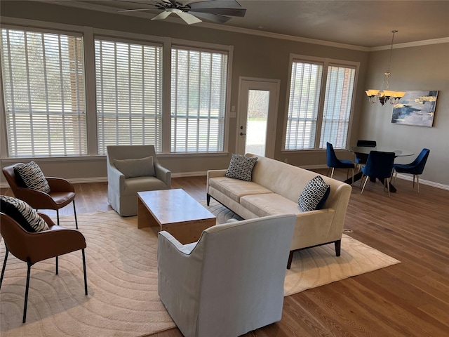 living room featuring baseboards, wood finished floors, ornamental molding, and ceiling fan with notable chandelier