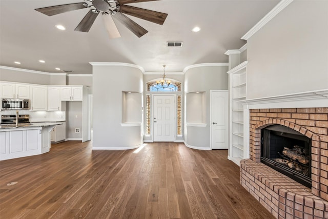 unfurnished living room featuring crown molding, a brick fireplace, ceiling fan with notable chandelier, and dark hardwood / wood-style flooring