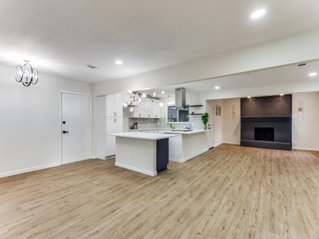 kitchen featuring white cabinetry, backsplash, island range hood, light hardwood / wood-style floors, and kitchen peninsula