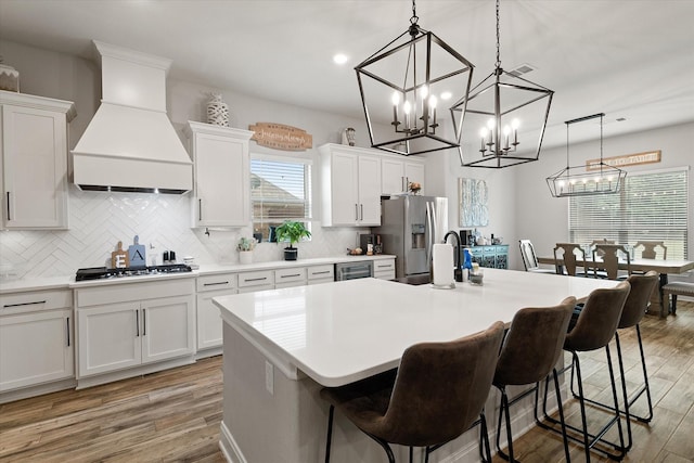 kitchen featuring a kitchen island with sink, white cabinets, and premium range hood