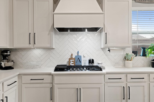 kitchen featuring tasteful backsplash, premium range hood, white cabinets, and stainless steel gas stovetop