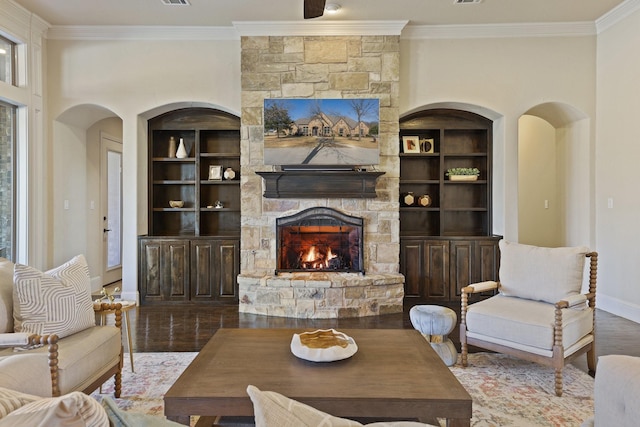 living room featuring crown molding, a stone fireplace, wood-type flooring, a wealth of natural light, and built in shelves