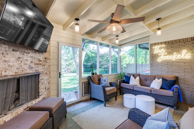 sunroom with beamed ceiling, ceiling fan, and a stone fireplace