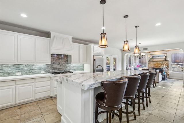 kitchen featuring white cabinetry, decorative backsplash, custom range hood, and a center island with sink