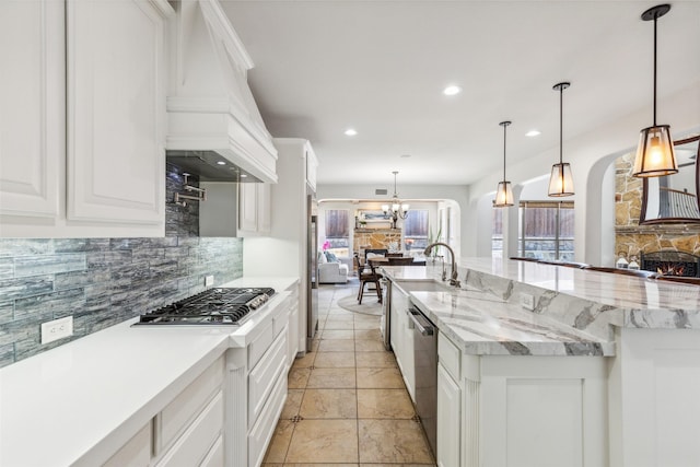 kitchen with light stone counters, a large island with sink, pendant lighting, stainless steel appliances, and white cabinets