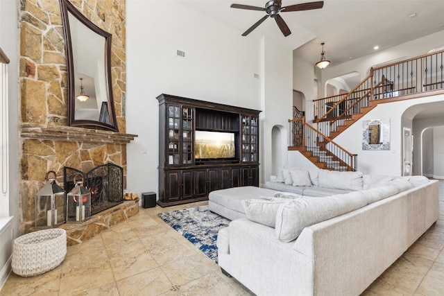 living room with a fireplace, ceiling fan, and a high ceiling