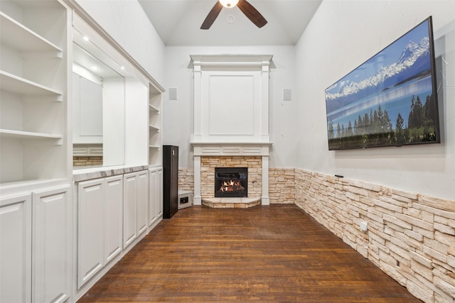 unfurnished living room with a stone fireplace, built in shelves, and ceiling fan