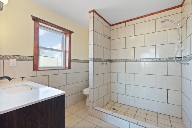 bathroom with toilet, tile walls, a tile shower, vanity, and tile patterned flooring