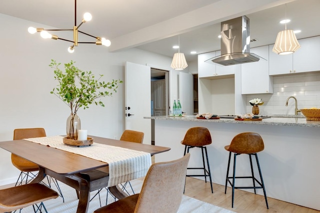 dining room featuring beamed ceiling, sink, and light hardwood / wood-style flooring