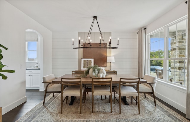 dining space featuring dark wood-type flooring, a chandelier, and wooden walls