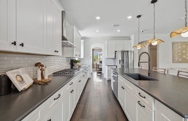 kitchen with sink, hanging light fixtures, stainless steel appliances, white cabinets, and wall chimney exhaust hood