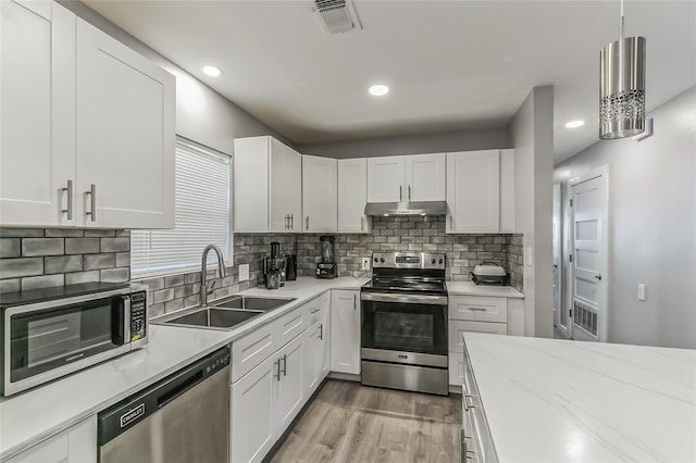 kitchen featuring sink, backsplash, stainless steel appliances, white cabinets, and decorative light fixtures