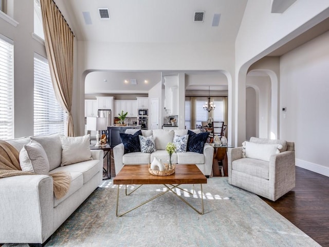 living room with a high ceiling, a healthy amount of sunlight, a notable chandelier, and dark hardwood / wood-style flooring