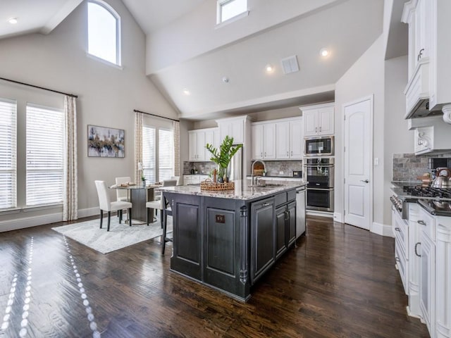 kitchen with tasteful backsplash, an island with sink, sink, white cabinets, and stainless steel appliances