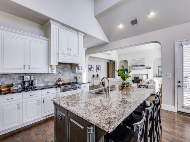 kitchen featuring stainless steel gas stovetop, a kitchen island with sink, dark stone countertops, and white cabinets