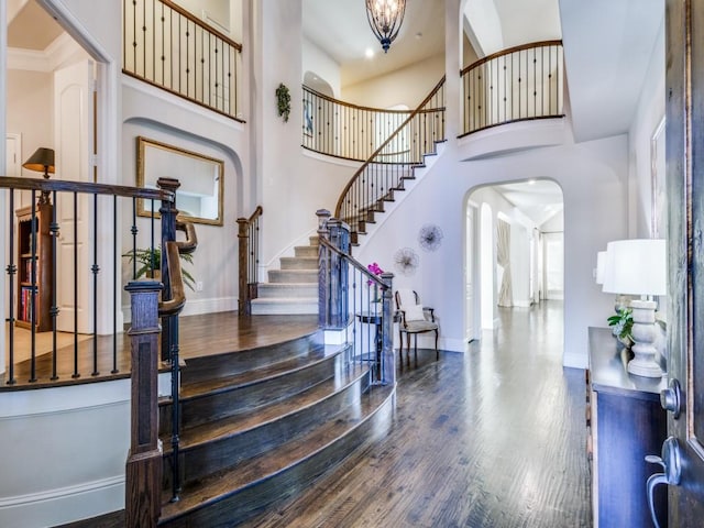 entrance foyer featuring hardwood / wood-style flooring, a towering ceiling, ornamental molding, and an inviting chandelier