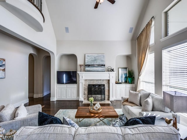 living room with ceiling fan, dark hardwood / wood-style floors, a fireplace, and a towering ceiling