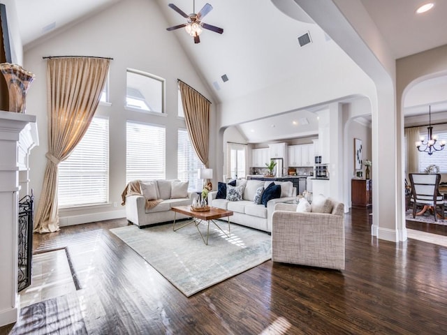 living room with ceiling fan with notable chandelier, a healthy amount of sunlight, dark wood-type flooring, and high vaulted ceiling