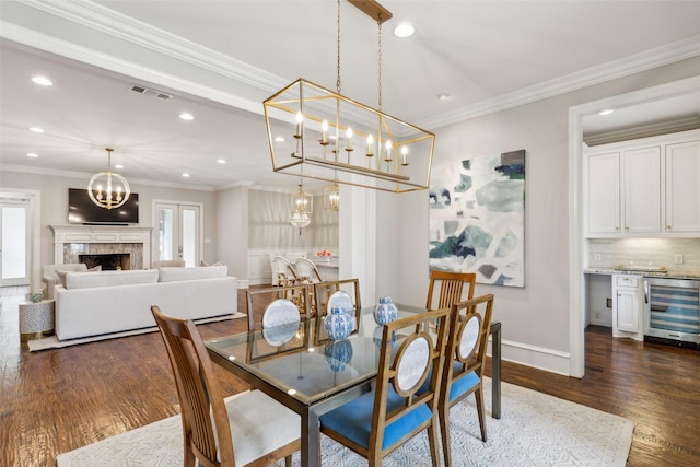 dining space featuring wine cooler, dark hardwood / wood-style flooring, ornamental molding, and a tile fireplace