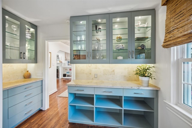 bar featuring dark hardwood / wood-style flooring, light stone countertops, and decorative backsplash