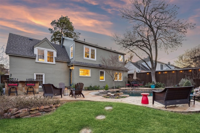 back house at dusk featuring a yard, a patio, and an outdoor bar