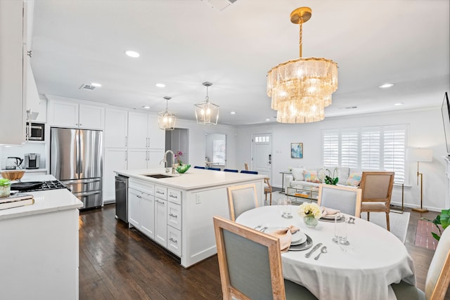 kitchen with sink, white cabinetry, decorative light fixtures, appliances with stainless steel finishes, and an island with sink