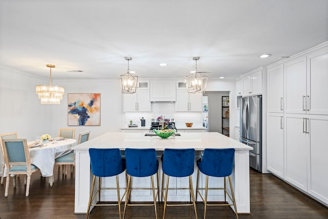 kitchen with a kitchen island with sink, pendant lighting, stainless steel appliances, and white cabinets