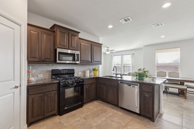 kitchen with appliances with stainless steel finishes, sink, backsplash, dark stone counters, and kitchen peninsula