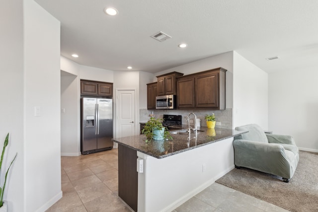 kitchen featuring sink, appliances with stainless steel finishes, dark stone countertops, decorative backsplash, and kitchen peninsula