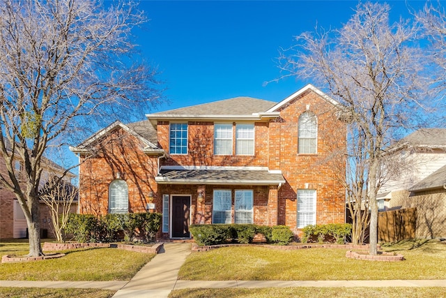 traditional home with a front yard, fence, brick siding, and a shingled roof