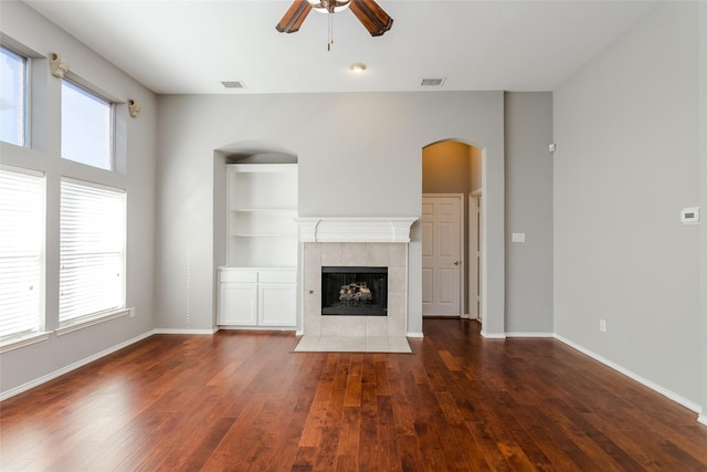 unfurnished living room featuring ceiling fan, dark hardwood / wood-style flooring, a tile fireplace, and built in features