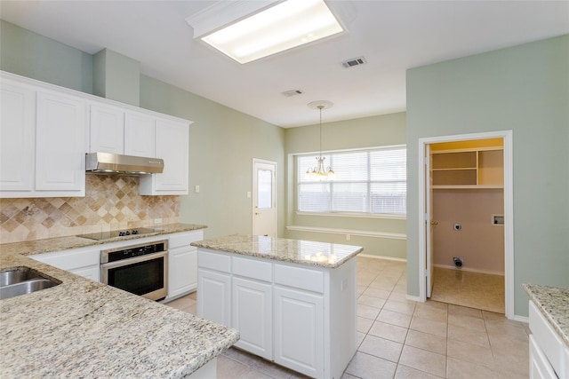 kitchen with hanging light fixtures, white cabinets, a kitchen island, decorative backsplash, and oven