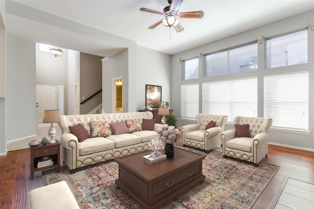 living room with ceiling fan, plenty of natural light, wood-type flooring, and a high ceiling