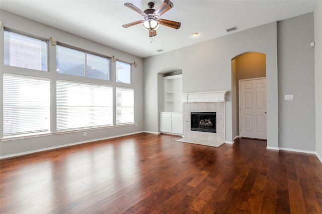 unfurnished living room with built in shelves, a fireplace, dark hardwood / wood-style floors, and ceiling fan