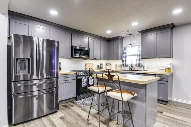 kitchen with a breakfast bar, butcher block counters, appliances with stainless steel finishes, pendant lighting, and light hardwood / wood-style floors