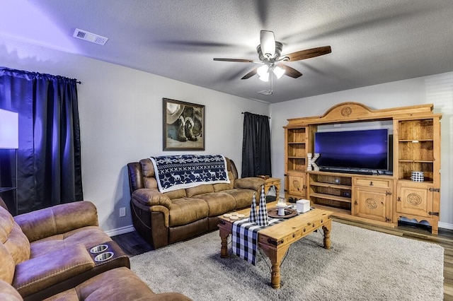 living area featuring visible vents, a textured ceiling, a ceiling fan, and wood finished floors