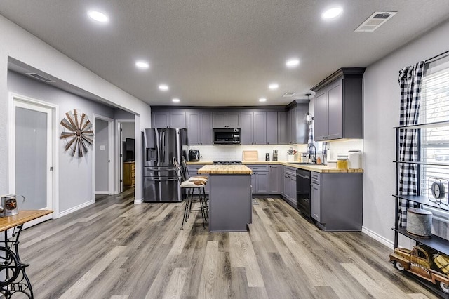 kitchen with gray cabinetry, stainless steel appliances, a kitchen breakfast bar, a kitchen island, and wood counters