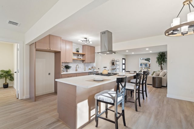 kitchen with pendant lighting, island exhaust hood, a kitchen island, stainless steel gas stovetop, and light wood-type flooring