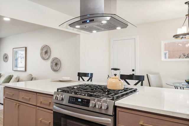 kitchen with hanging light fixtures, gas stove, island range hood, and a kitchen bar