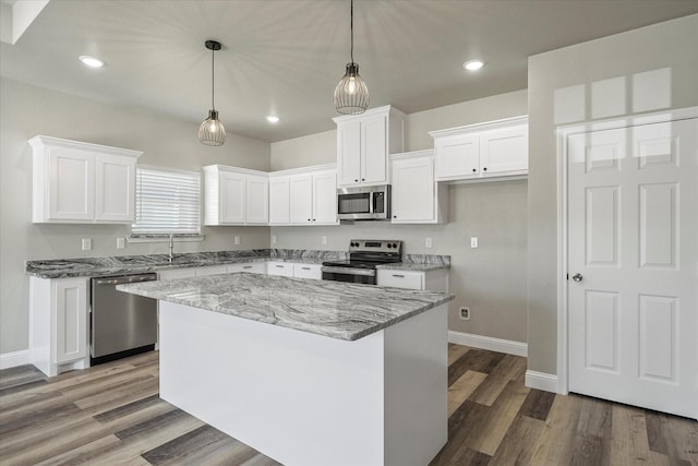 kitchen featuring a kitchen island, appliances with stainless steel finishes, pendant lighting, white cabinets, and light stone counters